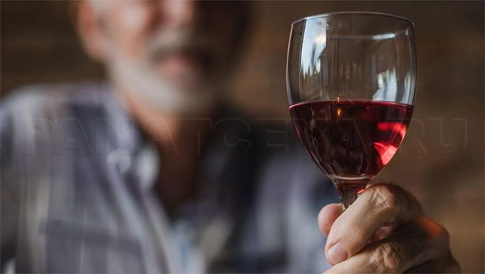 Пожилой мужчина держит бокал с вином